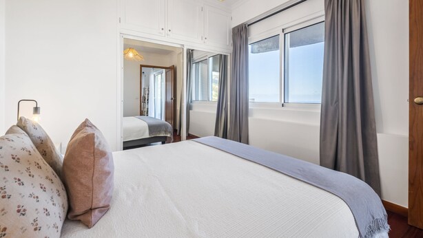 A bedroom with a large bed, a wardrobe, a mirror, and a window with curtains. - Casa da Ângela - By Wehost (Funchal)