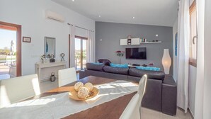A modern living room with a sofa, a dining table with a white tablecloth, and a flat-screen TV mounted on the wall. - Finca Monika Natalia (Mayorca)