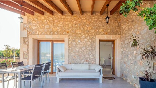A stone-walled room with a white sofa, dining table, and chairs. - Finca Monika Natalia (Mayorca)