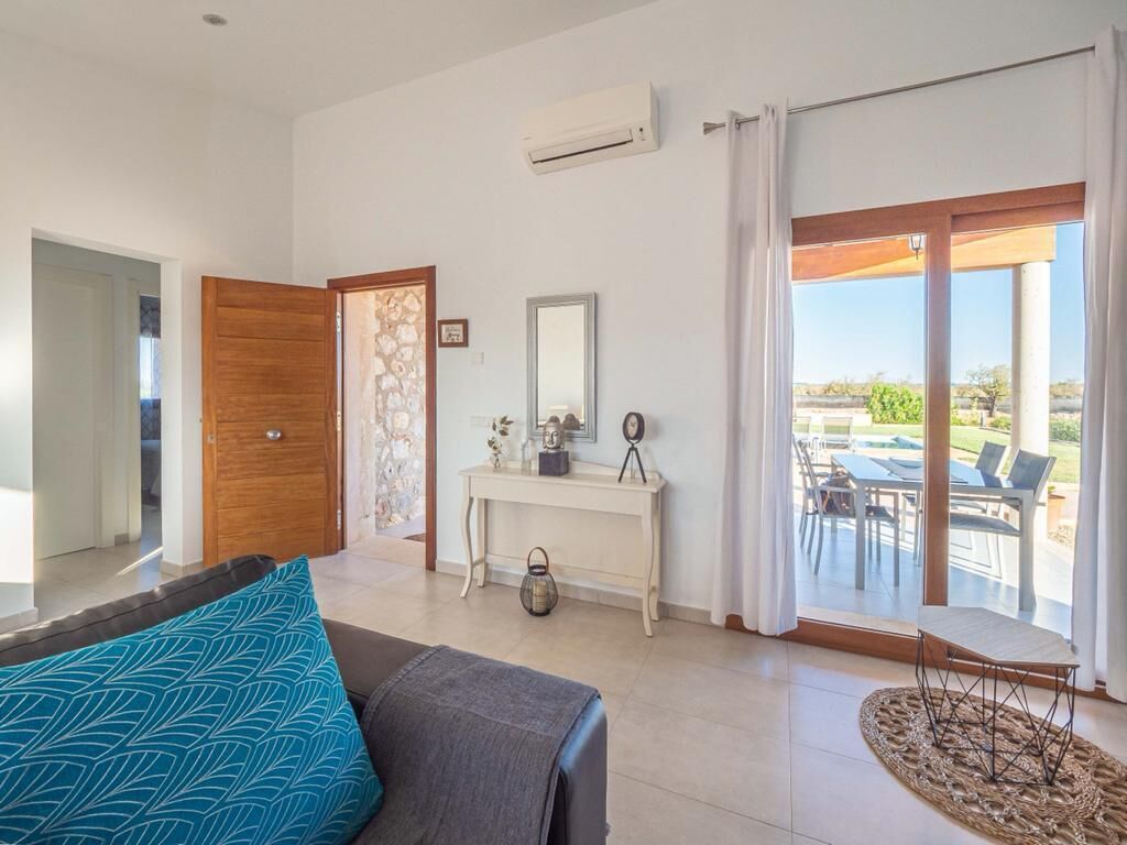 A modern hotel room with a bed, a console table with a mirror, a small table with chairs, and a large sliding glass door leading to an outdoor patio.