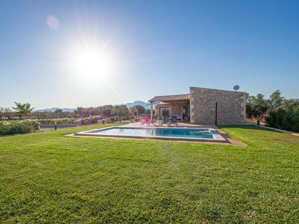 A modern house with a swimming pool, stone exterior, and a clear view of the mountains in the background.