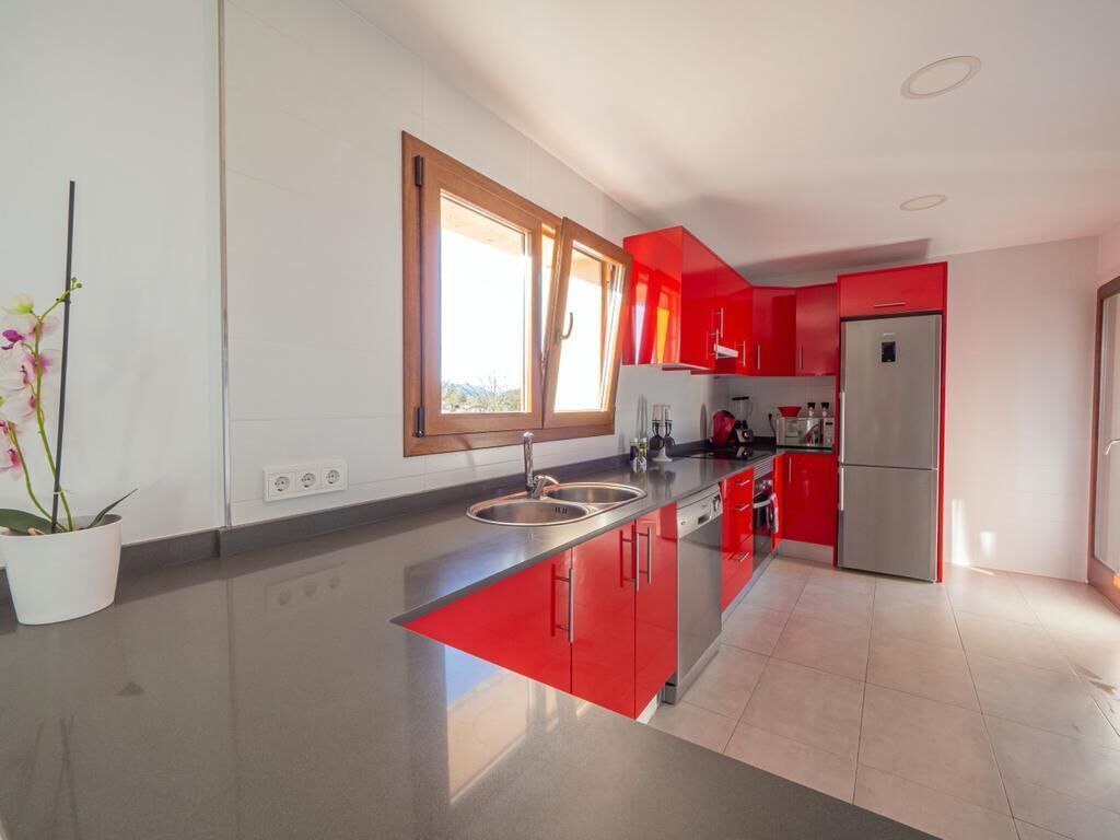 Una cocina moderna con armarios rojos, electrodomésticos de acero inoxidable y un ventanal grande.