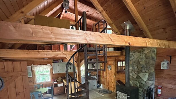 A rustic cabin interior with a loft bedroom, a stone fireplace, and a dining area. - The Rustic Woodzie at Elk Creek Escape (Hillsgrove)