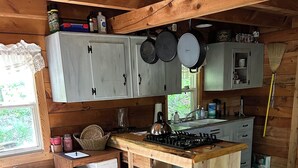 A wooden cabin kitchen with a central island, wooden cabinets, and a dining table with chairs. - The Rustic Woodzie at Elk Creek Escape (Hillsgrove)