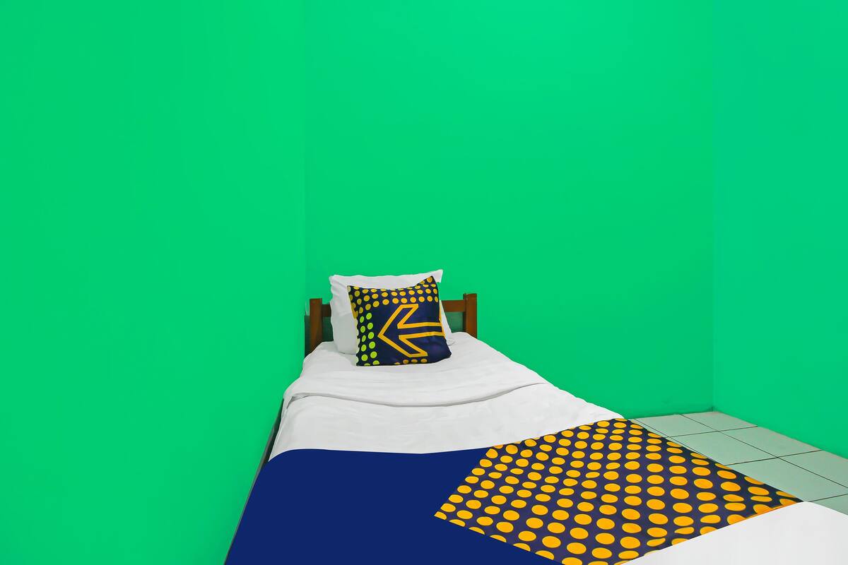 Un lit simple avec une couvre-lit blanche et bleue, un oreiller à motifs jaunes et bleus, et un mur vert.