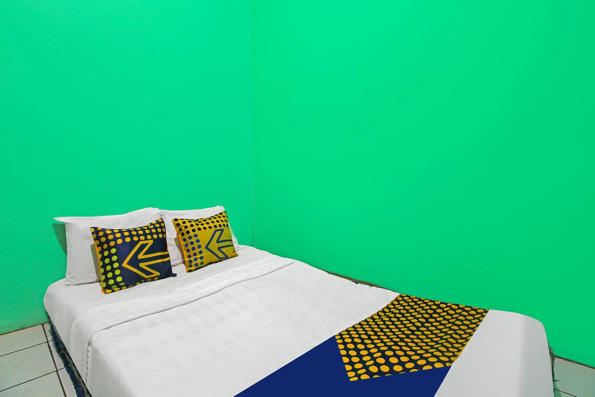 Un lit avec une literie blanche, deux oreillers aux motifs jaunes et bleus, et un plaid géométrique bleu et jaune.