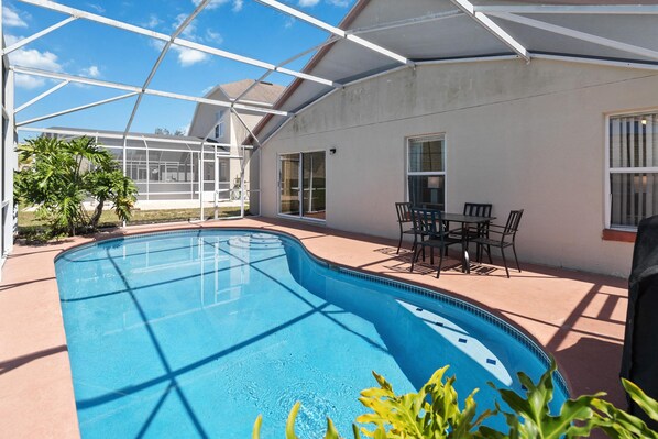 A swimming pool with a glass enclosure, patio furniture, and a small garden area. - Great Community, amazing private pool, near Disney! (Davenport)