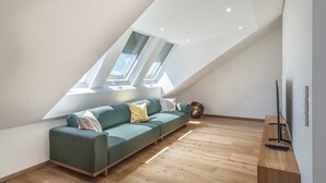 Une chambre de style loft moderne, avec un plafond en pente, un canapé vert, un plancher en bois et un meuble pour la télévision.