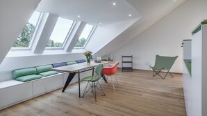 Une pièce moderne de style loft, dotée d’un plafond haut, de fenêtres de toit, d’une longue table à manger et d’une banquette intégrée avec des coussins.