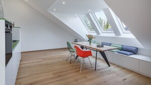 Un loft moderne avec un plafond en pente, un coin repas comprenant une table en bois et deux chaises, ainsi qu’un banc intégré avec des coussins.