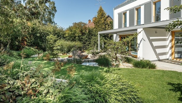 Une maison moderne dotée d’un jardin bien entretenu, comprenant un étang et diverses plantes.