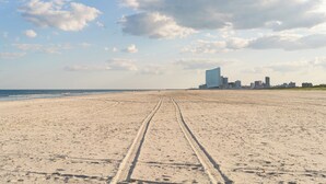 Een breed zandstrand met sporen van banden die naar een stadslijn in de verte leiden.