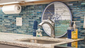Een keuken met een roestvrijstalen spoelbak, een decoratieve spatwand in blauw en wit, en een rol keukenpapier.