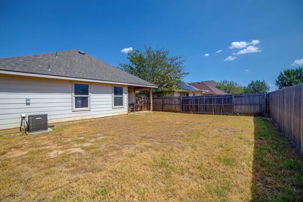 A residential backyard with a house, a fenced area, and a tree.