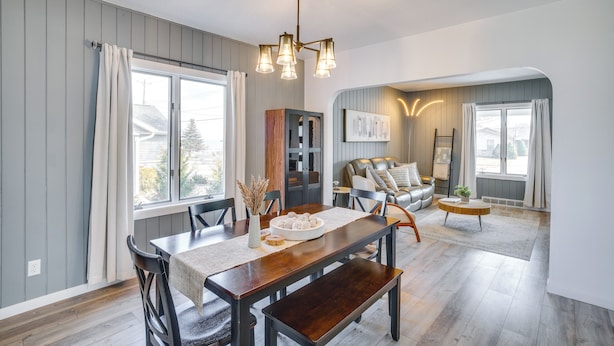 A dining area with a wooden table, chairs, and a chandelier. There is a sofa and a coffee table in the background. - Steps to Lake Michigan: Manitowoc Home w/ Fire Pit (Manitowoc)