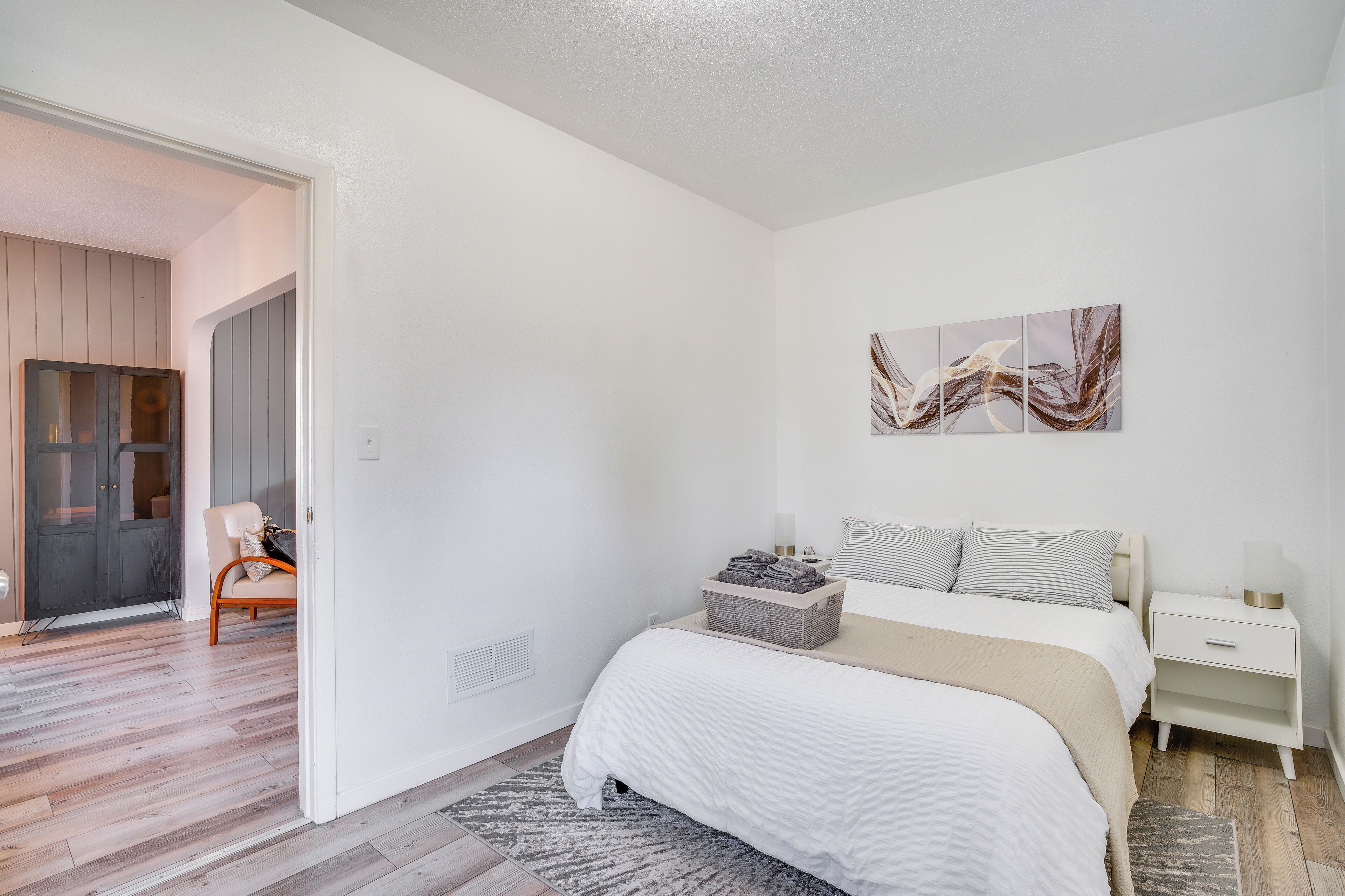 A bedroom with a bed, bedside tables, a wall art piece, and a door leading to another room.