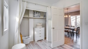A room with a wooden floor, a white dresser, a laundry basket, and a door leading to a dining area with a table and chairs. - Steps to Lake Michigan: Manitowoc Home w/ Fire Pit (Manitowoc)