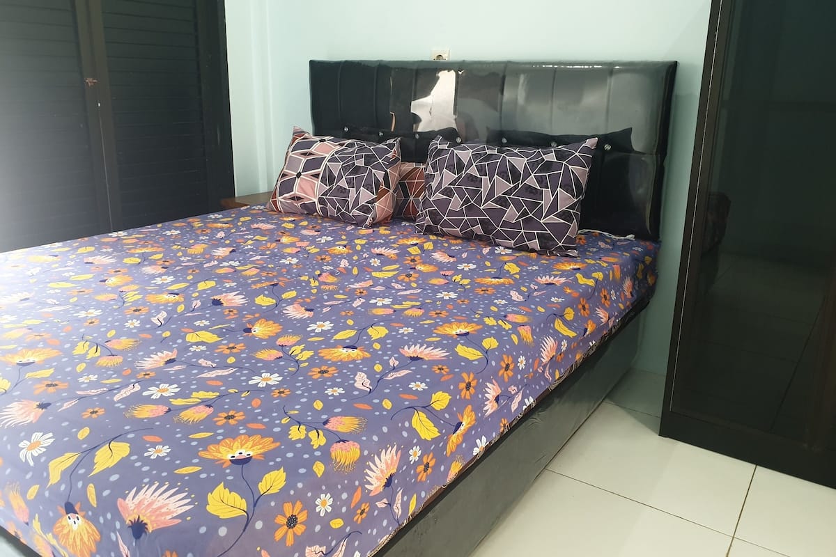 Ein Bett mit einem blumigem Überwurf, zwei geometrisch gemusterten Kissen und einem dunklen Kopfteil.