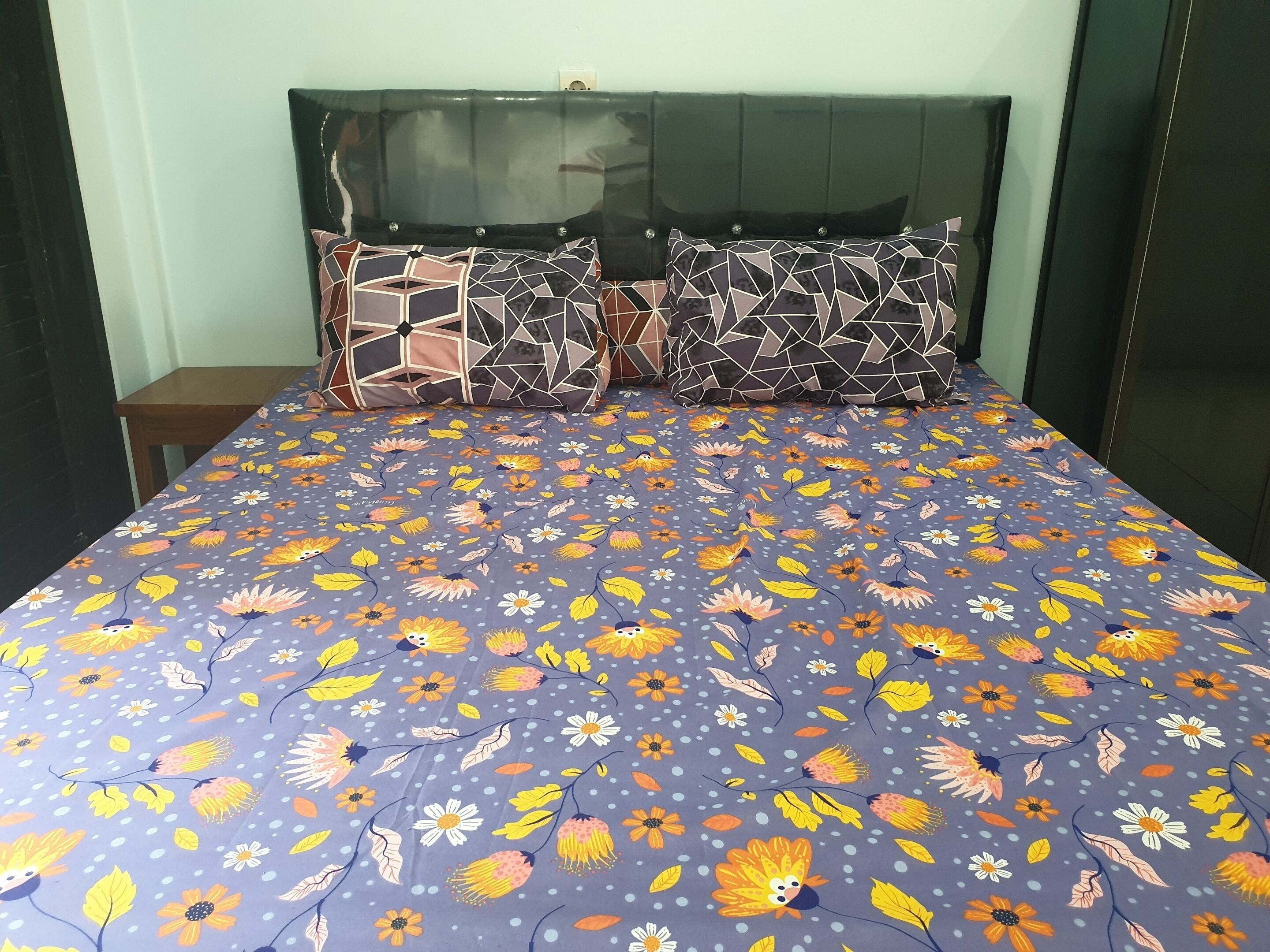 A bed with a floral-patterned bedspread, a wooden nightstand, and a headboard with a mirror.