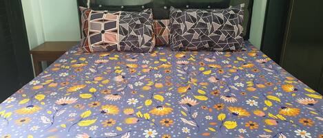 A bed with a floral-patterned bedspread, a wooden nightstand, and a headboard with a mirror.