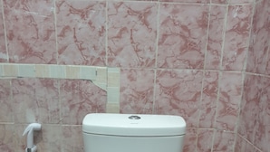 A bathroom with a white toilet, pink marble tiles, and a tiled floor.