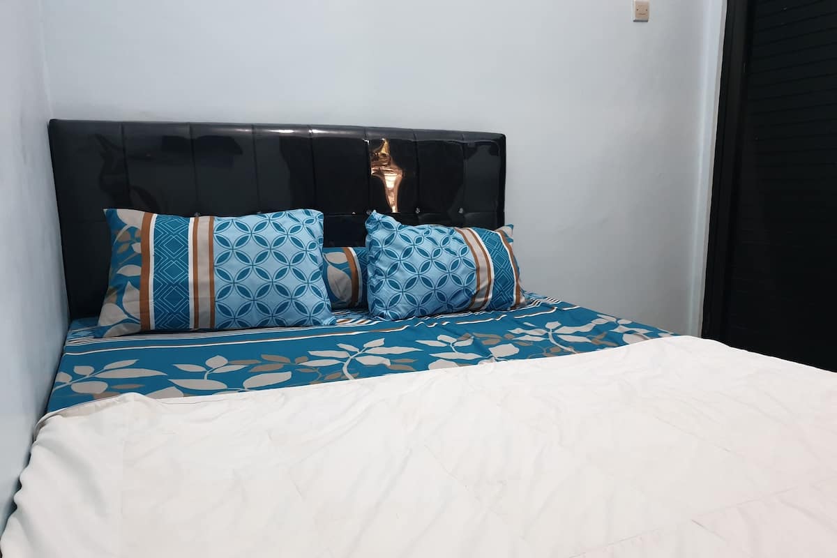 Ein ordentlich bezogenes Bett mit einer blauen und weißen Bettdecke mit Muster, zwei passende Kissen und ein schwarzes Kopfteil.