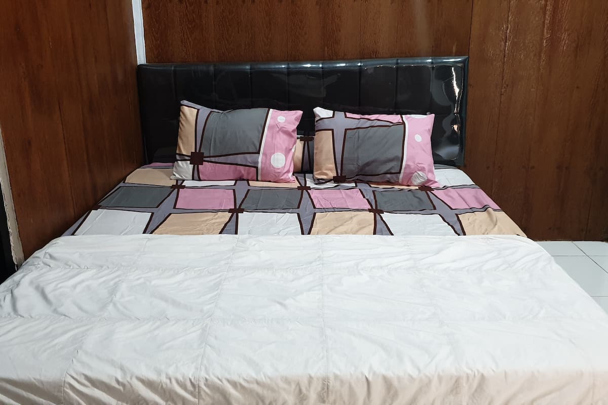 Ein ordentlich bezogenes Bett mit einem gemusterten Überwurf und Kissen, einem schwarzen, mit Stoff bezogenen Kopfteil und einem Fliesenboden.