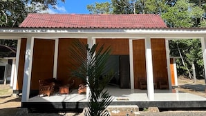 A two-story building with a red-tiled roof, a covered porch with wooden furniture, and a small garden area in front.