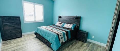 A bedroom with a bed, a ceiling fan, a window, and a dark wooden headboard.