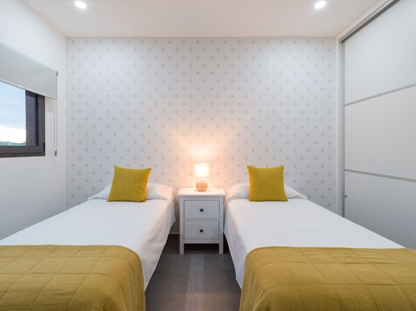 Una habitación con dos camas, una mesita de noche con lámpara y una ventana.