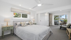 Quarto com cama, mesas de cabeceira, ventoinha no teto, janela com vista e porta de vidro deslizante para uma varanda.