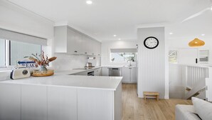 Cozinha moderna com armários brancos, uma ilha central e uma área de refeições com escada.