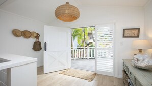 Um interior claro com uma porta de madeira que dá para uma varanda, uma luminária de palha no teto e uma citação emoldurada na parede.