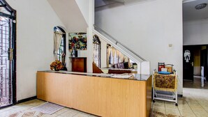 A reception area with a wooden counter, a staircase, and a cart with a patterned cover. - Hotel O Mw 46 Guesthouse (Yogyakarta)