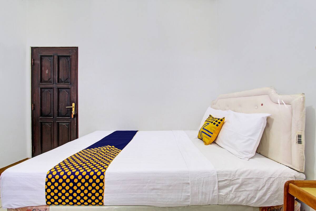 A bed with a white and blue bedspread, a yellow and blue pillow, and a wooden chair.
