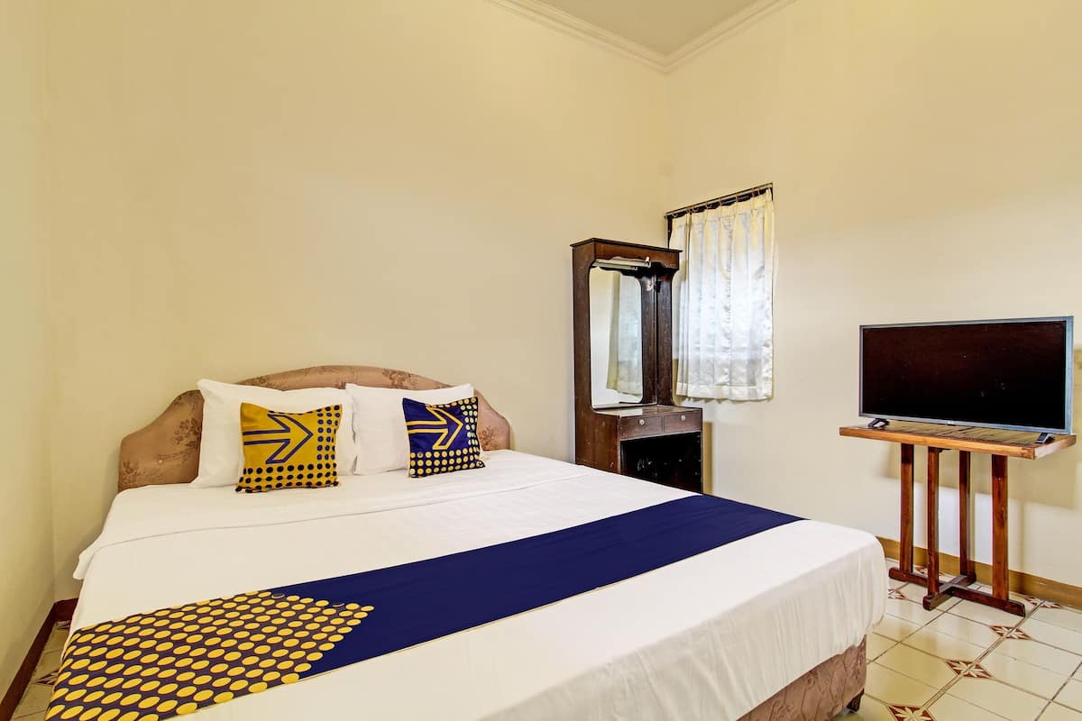 A hotel room with a bed, a TV on a stand, and a mirror on the wall.