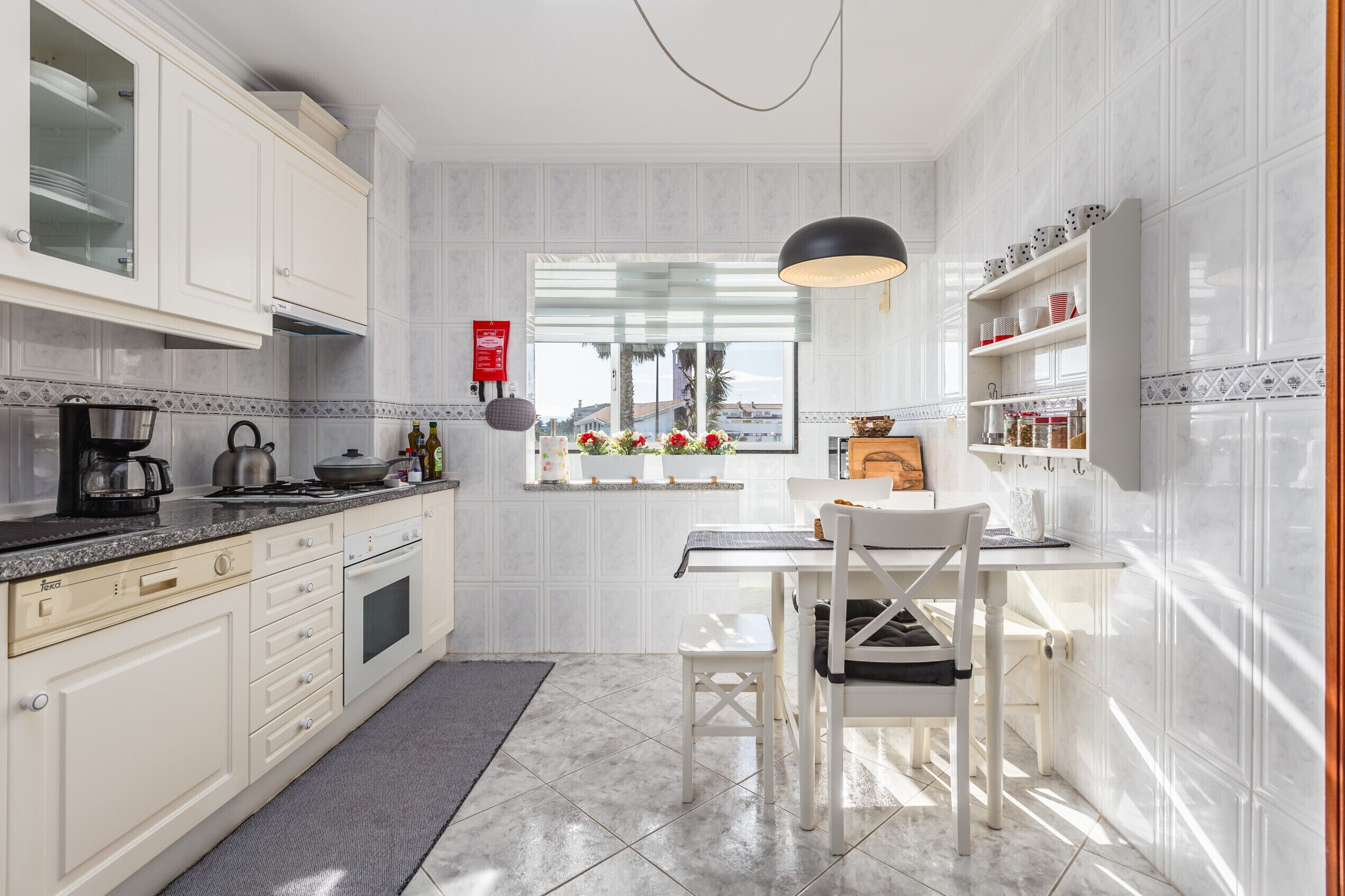 Een moderne keuken met witte kasten, een eethoek met tafel en stoelen, een raam met uitzicht en een hangende吊灯.