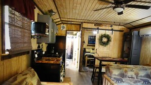 L’intérieur chaleureux d’un chalet avec un plafond en bois, un coin cuisine équipé d’une cuisinière et d’un four à micro-ondes, une table à manger et deux canapés à motifs.