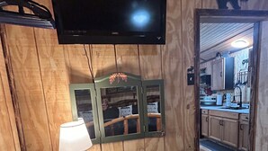 Une pièce aux murs lambrissés, avec un téléviseur fixé au mur, un bureau avec une lampe et un miroir au-dessus.
