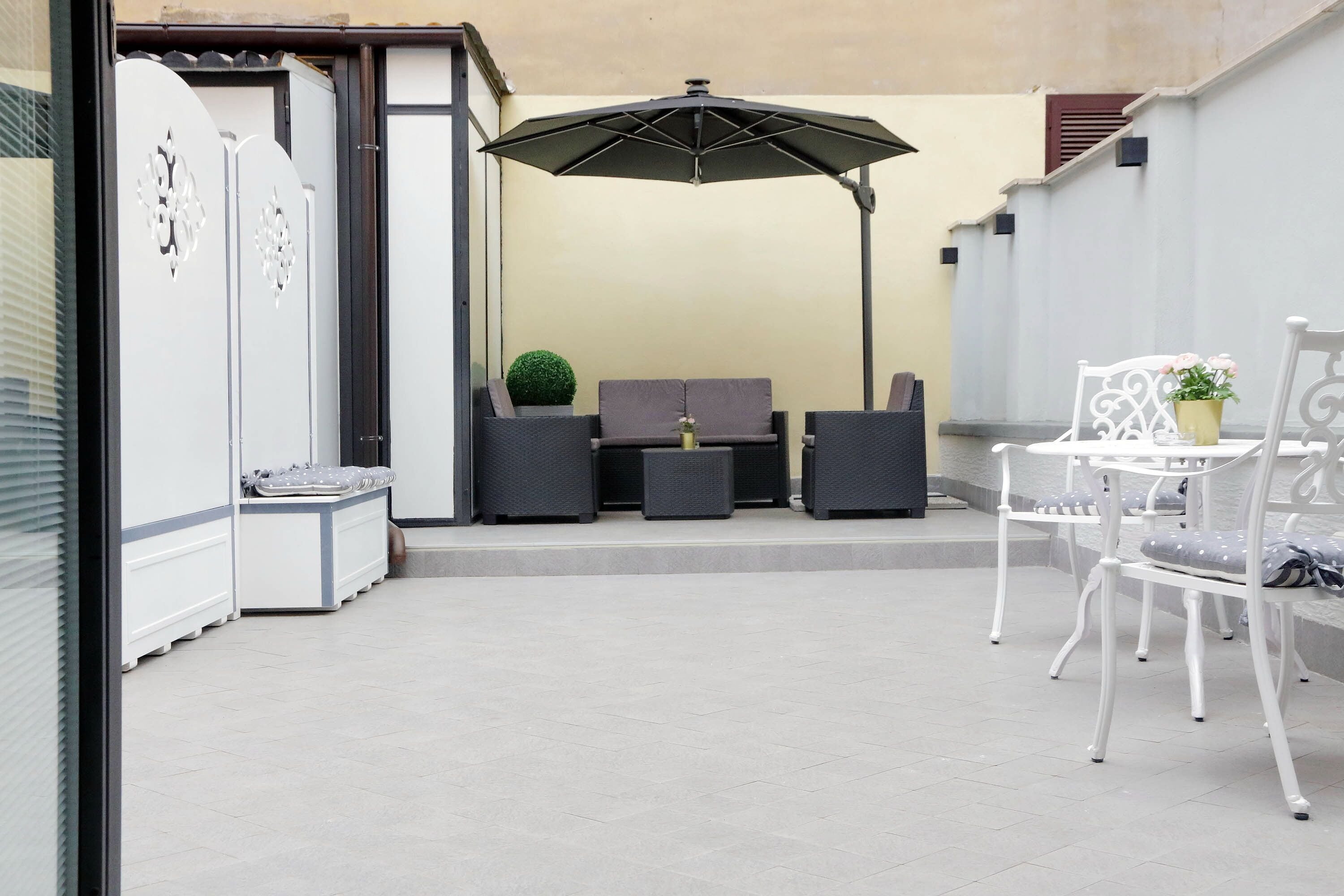 Un espace extérieur aménagé en terrasse, avec un coin salon comprenant un canapé, deux fauteuils et une petite table sur laquelle est posée une plante en pot.