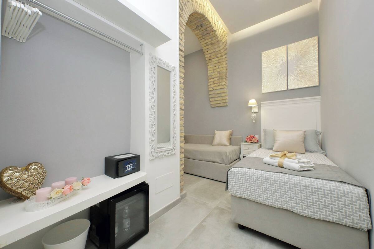 A modern bedroom with a bed, a TV, a small table with decorative items, and a stone archway.