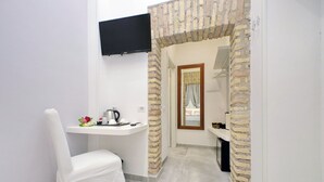 A narrow hallway with a white chair, a small table with a kettle, and a television mounted on the wall. - Roman Holiday Suites (Rome)