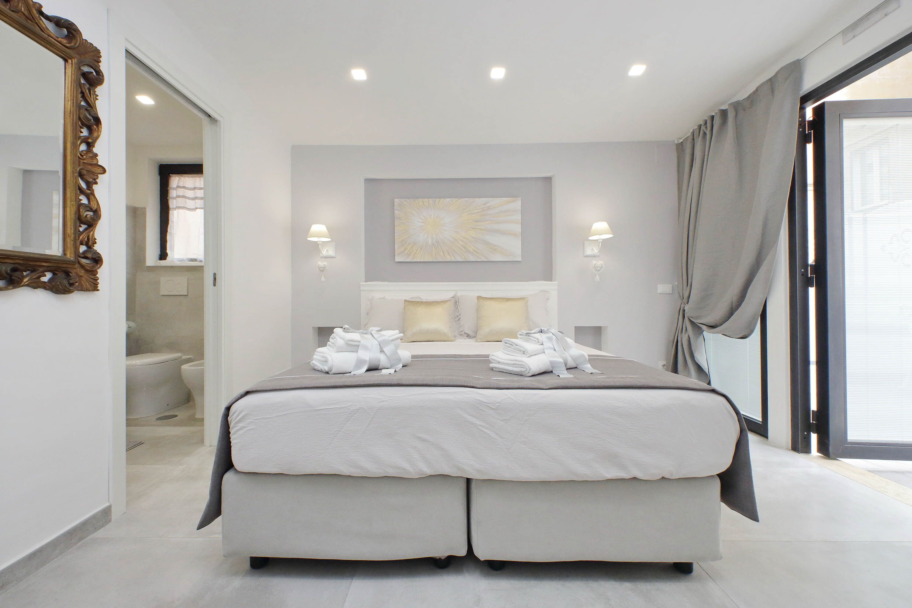 A modern bedroom with a large bed, two bedside lamps, a decorative wall piece, and a view through a glass door.