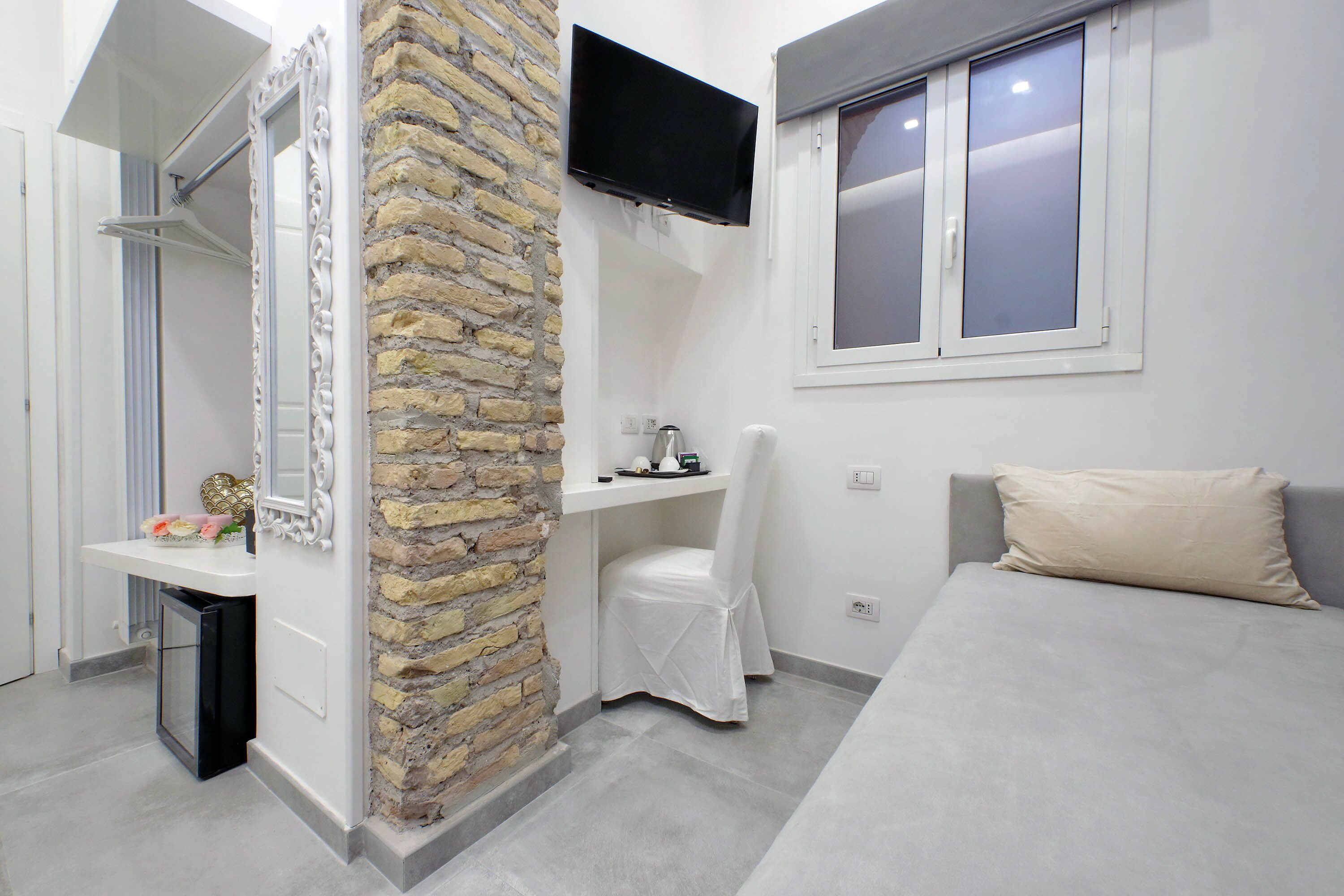 A bedroom with a bed, a TV mounted on the wall, a window, and a stone wall.