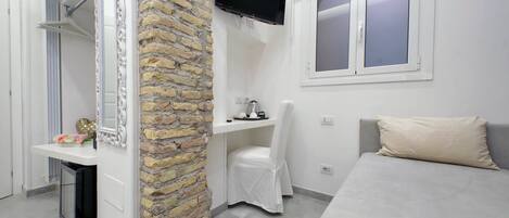 A bedroom with a bed, a TV mounted on the wall, a window, and a stone wall.