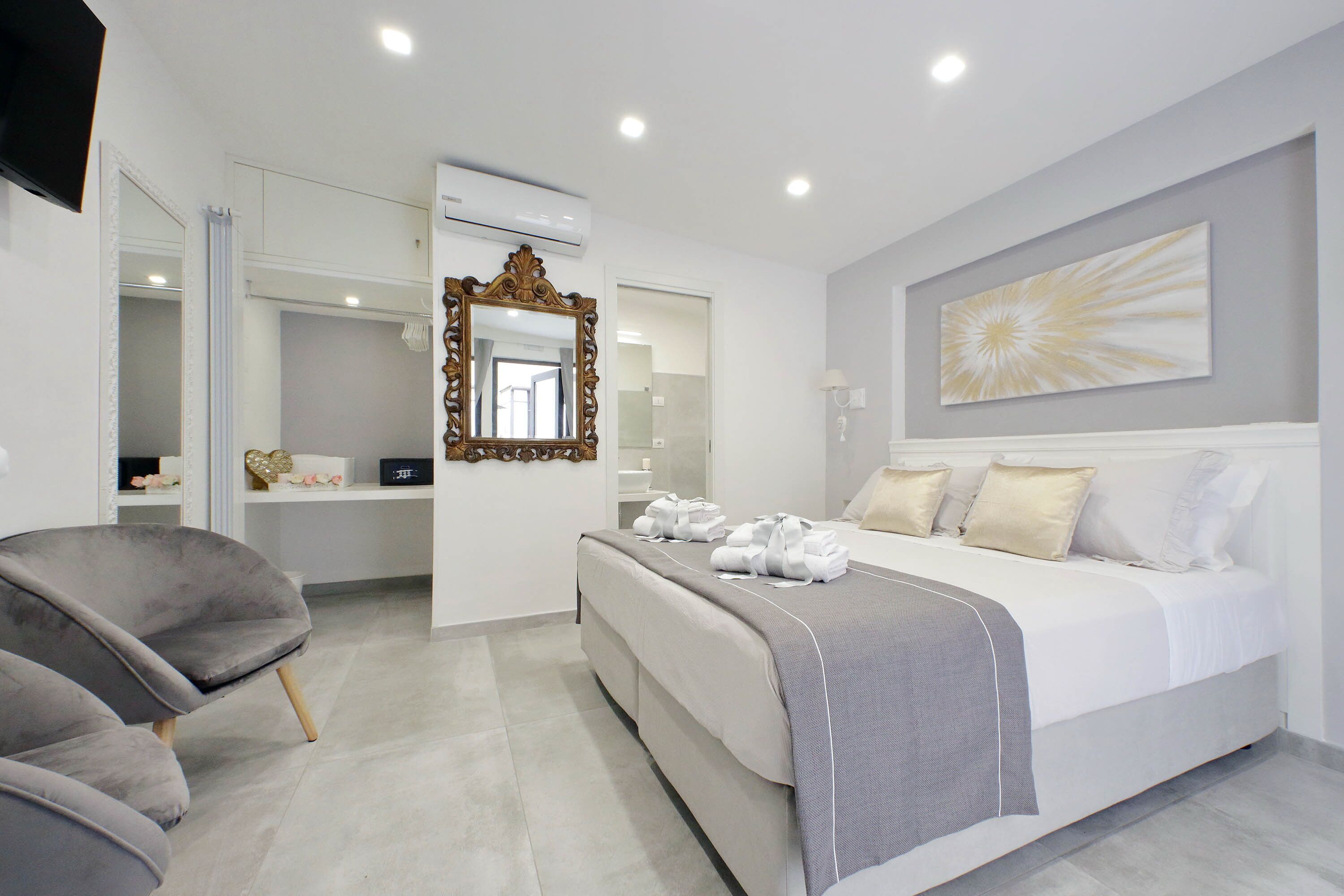 A modern bedroom with a large bed, a vanity with a mirror, and a grey armchair.