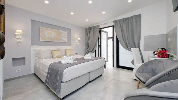 A modern bedroom with a bed, bedside tables, and a seating area. - Roman Holiday Suites (Rome)