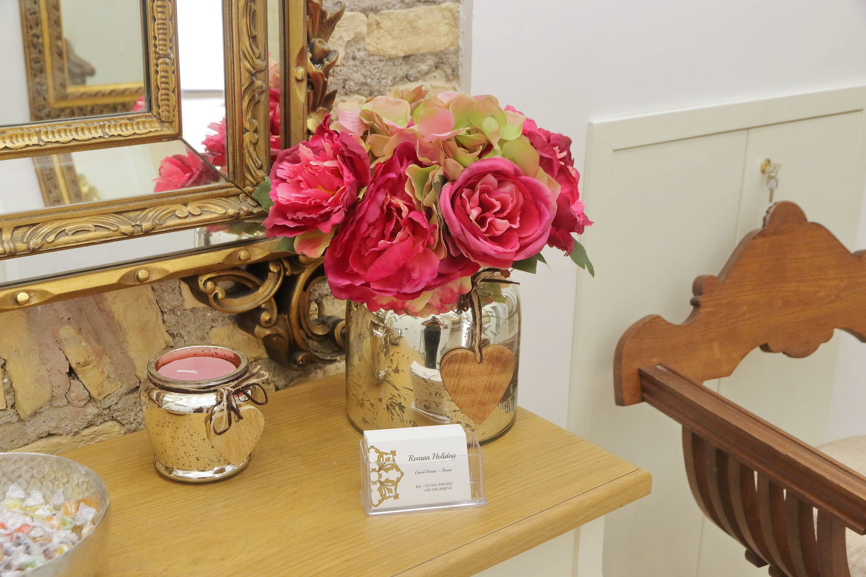 A wooden table with a vase of pink flowers, a candle, and a small card.