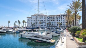 Un port de plaisance avec des bateaux amarrés, un bâtiment blanc doté de balcons et des palmiers.