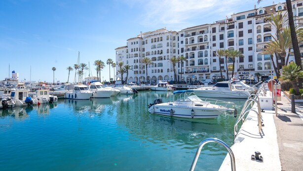 Un port de plaisance avec des bateaux amarrés, un bâtiment blanc doté de balcons et des palmiers.